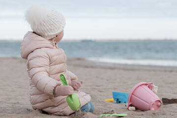 Cute little girl is digging in the sand on a cold day at the beach - Powered by Adobe