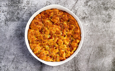 Breakfast Strata casserole with ham, herbs, cheese and cream in a white baking dish on a dark grey...