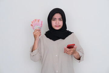 Young moslem girl holding money and handphone showing confused expression - obrazy, fototapety, plakaty