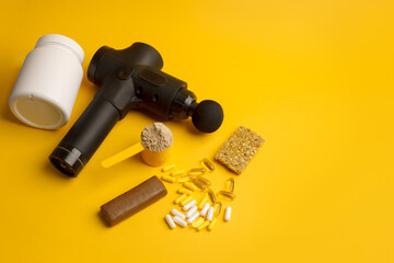 Therapeutic percussive massage gun, fit meal, pills, sport energy bar, protein on yellow background...