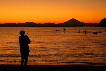 Fototapeta na wymiar 夕暮れの逗子海岸、オレンジ色に染まる海でカヤックを楽しむ若者