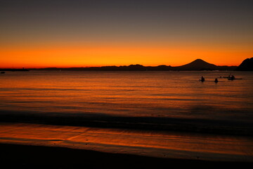 夕暮れの逗子海岸、オレンジ色に染まる海でカヤックを楽しむ若者