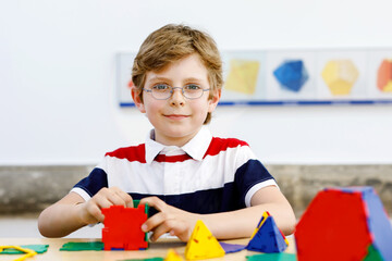 Happy kid boy with glasses having fun with building and creating geometric figures, learning...