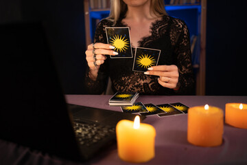 young woman in black witch clothes sit in dark office or cabinet and work on laptop, concept small women's business, tarot card and divination