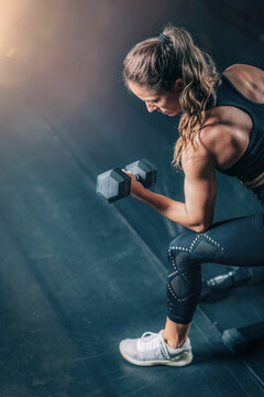 Female Athlete Exercising with Dumbbells in the Gym.