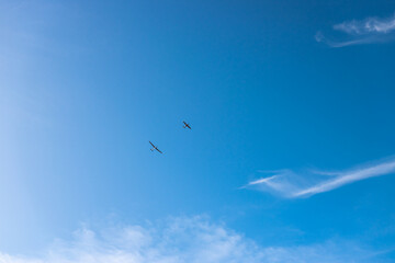 Silhouette of a plane pulling a glider against blue sky with some clouds. .