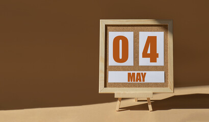 May 4th. Day 4 of month, Calendar date. Cork board, easel in sunlight on desktop. Close-up, brown background. Spring month, day of year concept