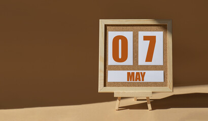 May 7th. Day 7 of month, Calendar date. Cork board, easel in sunlight on desktop. Close-up, brown...