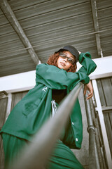 Fashion, street style and woman with green clothes, sunglasses and hat standing on stairs of an urban city building. Portrait of a cool female, hip hop or fashionable hipster model with casual outfit