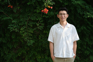 Smiling Asian young man with glasses, in front of Campsis grandiflora (Chinese trumpet vine) flower