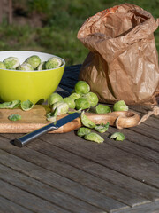 Vertical shot of Brussels sprouts on a wooden cutting board with a knife a brown paper bag and a green bowl