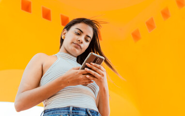 Portrait of attractive latin girl messaging on cell phone. Low angle of a beautiful Latin girl...