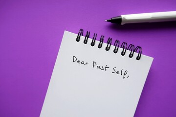 Notebook and pen on purple background with handwritten text DEAR PAST SELF,  self reflection letter...