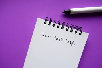 Notebook and pen on purple background with handwritten text DEAR PAST SELF,  self reflection letter to the person you were, advice to give your past self to tell them about what happened then and now