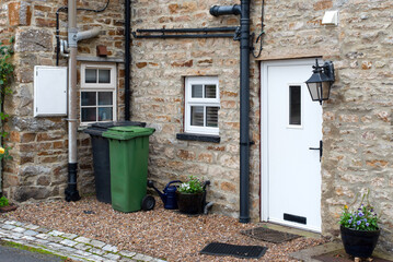 A Green and a black wheelie bin in front of a house entrance somewhere in a small village near Leyburn, Yorkshire, UK. - obrazy, fototapety, plakaty