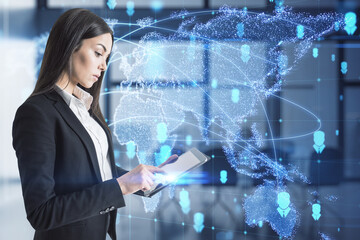 Attractive european businesswoman using tabet with abstract glowing map hologram on blurry office interior background. Digital world, transformation and future cyber space concept. Double exposure.