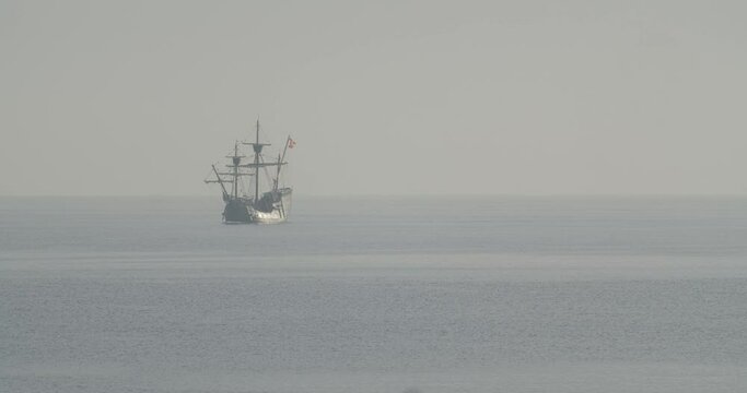 Ferdinand Magellan Nao Victoria carrack boat replica with spanish flag sails in the mediterranean at sunrise in calm sea exiting the frame in slow motion 60fps
