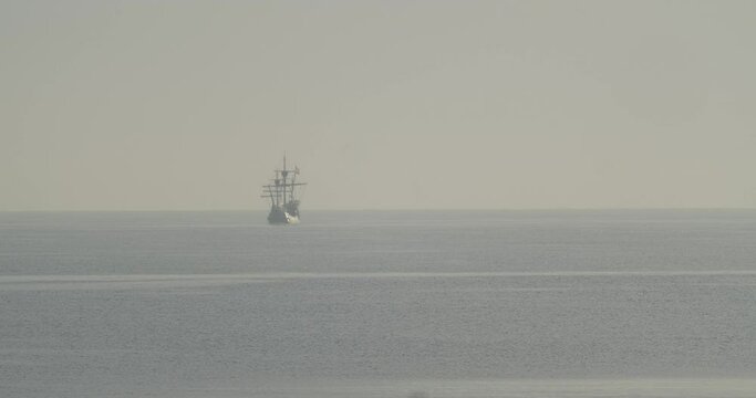 Ferdinand Magellan Nao Victoria carrack boat replica with spanish flag sails in the distance in the mediterranean at sunrise in calm sea in slow motion 60fps
