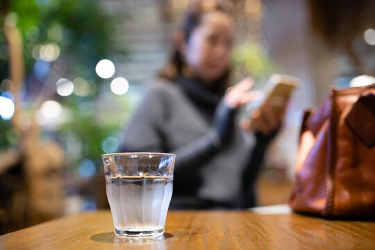 テーブルに置かれた水の入ったコップとスマートフォンを見る女性
