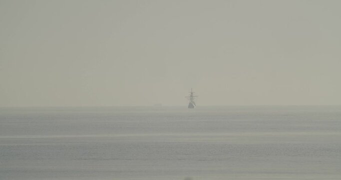 Ferdinand Magellan Nao Victoria carrack boat replica sails in the distance in the mediterranean at sunrise in calm sea in slow motion 60fps