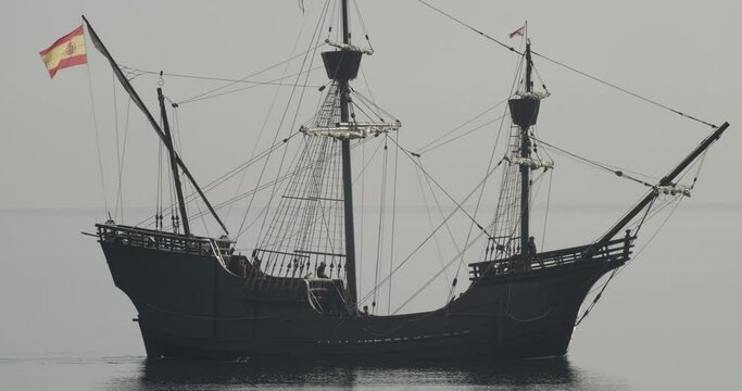 Ferdinand Magellan Nao Victoria carrack boat replica with spanish flag sails in the mediterranean at sunrise in calm sea side shot in slow motion 60fps