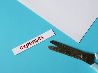 Scissors on blue background cutting paper piece with handwritten text EXPENSES, means to cut or...