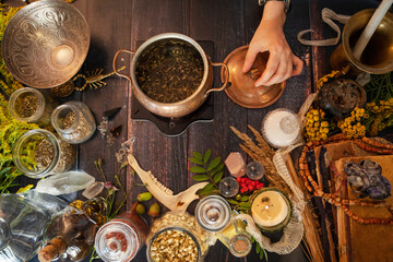Soft focus. Cauldron with warm herbal infusion on the wooden table. Hand holding the lid. Copper pot with herbs for ritual cleansing. A special blend of plants used for Ceremonies and spells. Top view