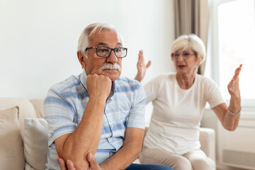 Senior couple having argument on the couch at home in the living room. Woman and man emotions gesturing with hands. Senior couple arguing