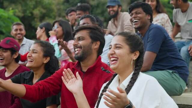 Group of audience laughing while watching cricket sports match at stadium by showing thumbs down gesture - concept of entertainment, teasing and making fun of players.