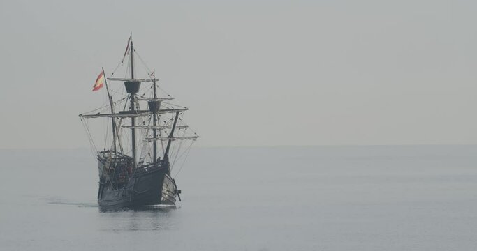 Ferdinand Magellan Nao Victoria carrack boat replica with spanish flag sails in the mediterranean at sunrise in calm sea front shot in slow motion 60fps