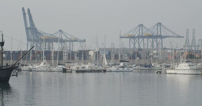 Ferdinand Magellan Nao Victoria carrack boat replica with spanish flag going into harbour in Valencia with cranes in the background in slow motion 60fps