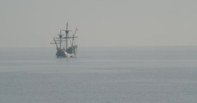 Ferdinand Magellan Nao Victoria carrack boat replica with spanish flag sails in the mediterranean at sunrise in calm sea exiting the frame in slow motion 60fps