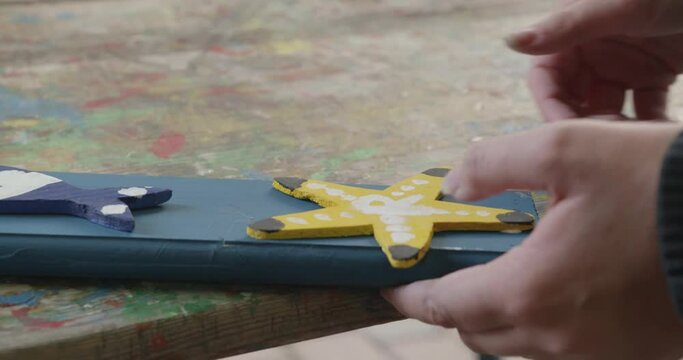 Teenager glues a sawed out and painted wooden star onto a fence rail