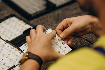 Close up of african man's hands with tongs and wires, working with electric sceme for LED lamps. He is sitting at his working table, wearing uniform