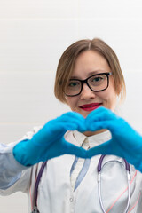 Beautiful young happy doctor woman in medical gloves and glasses with a stethoscope in the hospital shows hand gestures. Selective focus. Portrait. Close-up