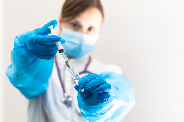 Young woman doctor in a medical mask and gloves with a syringe in her hand and a stethoscope in a hospital during a coronavirus pandemic. Selective focus. Portrait