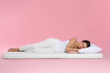 Young woman lying on soft mattress against pink background
