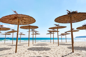 Beach wooden umbrellas on sand by sea
