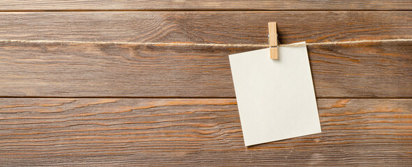 An empty piece of paper is hanging on a rope. A design element. Brown wooden background. Copy space.