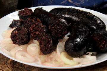 Baked black pudding with pickled onions on a white plate. Sliced and fried blood sausage on a plate