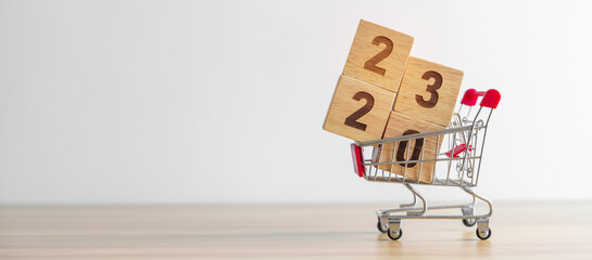 Happy new year with 2023 block in shopping trolley cart on table. E commerce, online shopping,...