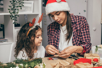 Mother and little daughter are preparing for Christmas,packing and decorating gifts at...