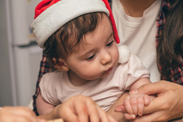 Mother is holding a baby in a Santa hat at home.Preparing for Christmas.Upcoming winter holidays and celebrations.