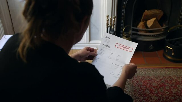 An unrecognizable female opening a debt letter. The woman is reading a rent overdue notice at home