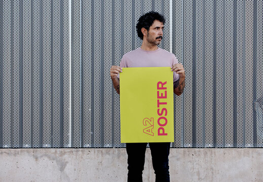 Man Holding A2 Poster Mockup in front a Metallic Wall