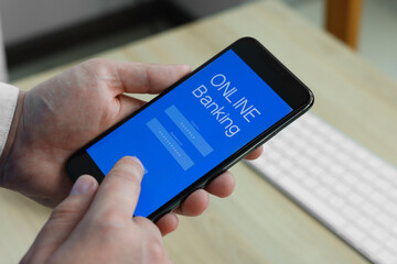 Man using online banking app on smartphone at wooden office table, closeup
