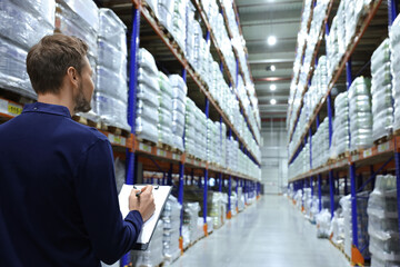 Manager holding clipboard in warehouse with lots of products, back view. Space for text