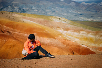 Cheerful woman sits on red altai mountains background. Happy female traveller enjoying vacation in fantastic place in siberia. Sightseeing, wanderlust concept.