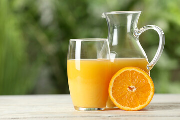 Tasty orange juice in glass and jug on white wooden table against blurred background. Space for text