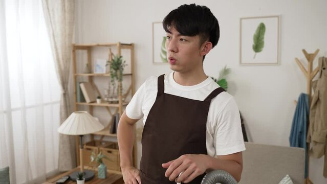 slow motion of a perspiring asian male wiping sweat on forehead and looking into distance with a sigh of relief after finishing the housecleaning work at home